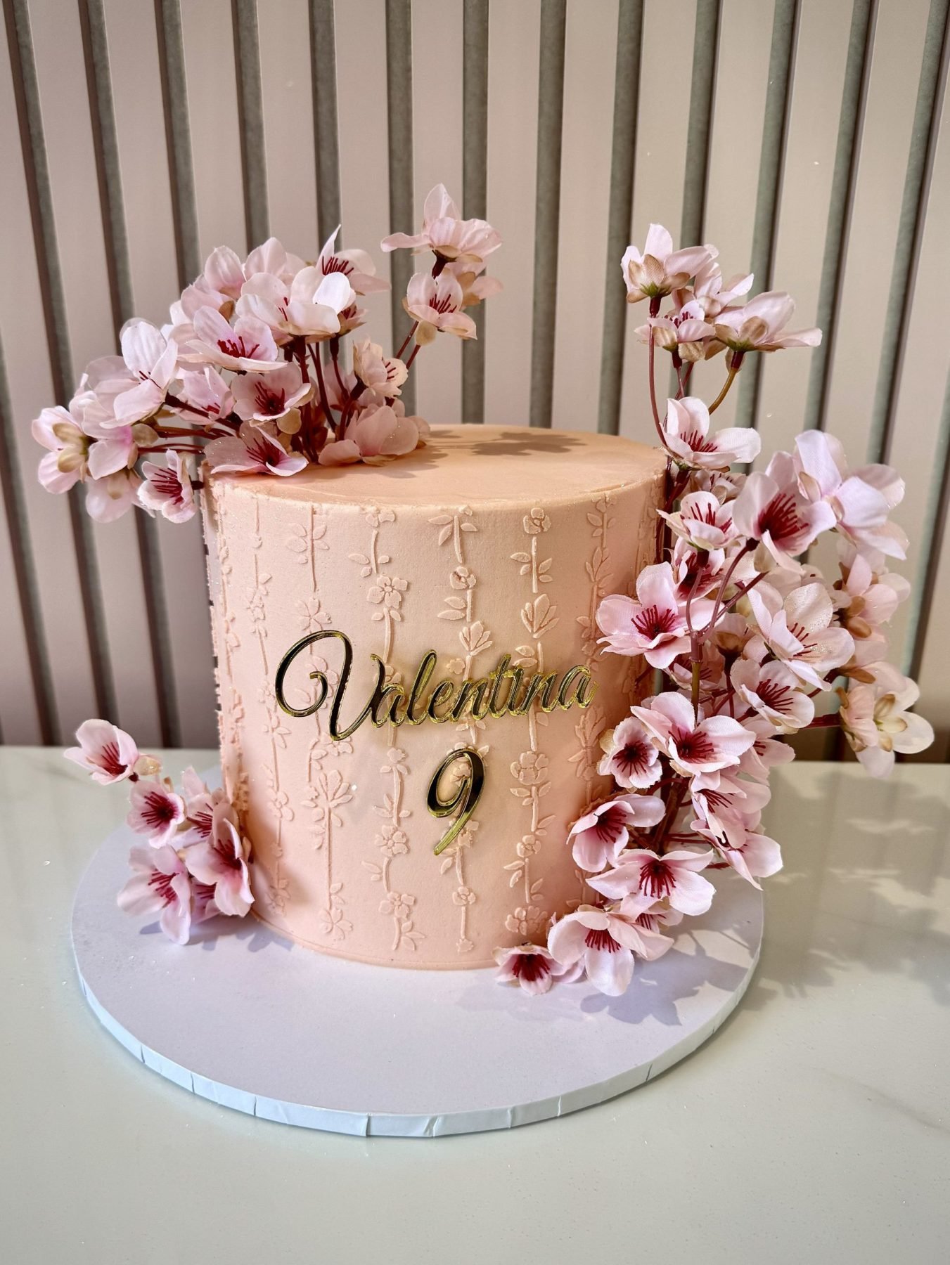 Pink cherry blossom birthday cake with buttercream finish, floral embossing and cascading blossom decorations