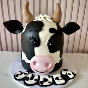 Cute cow birthday cake with black and white fondant design, pink snout and playful character features