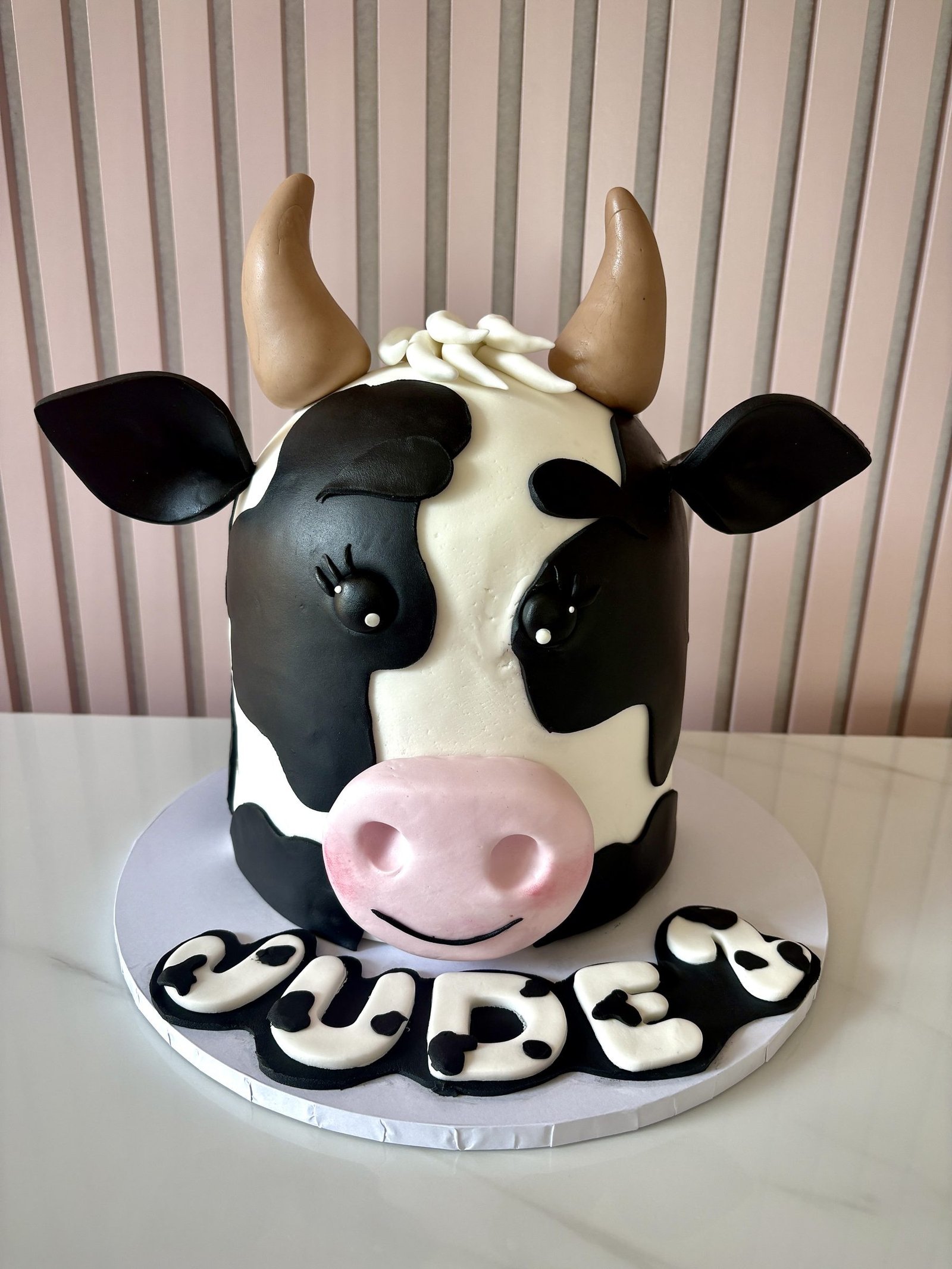 Cute cow birthday cake with black and white fondant design, pink snout and playful character features