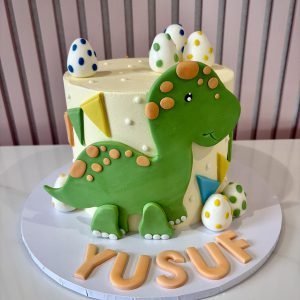 Cute green dinosaur birthday cake with fondant dinosaur, colourful spotted eggs and soft buttercream finish