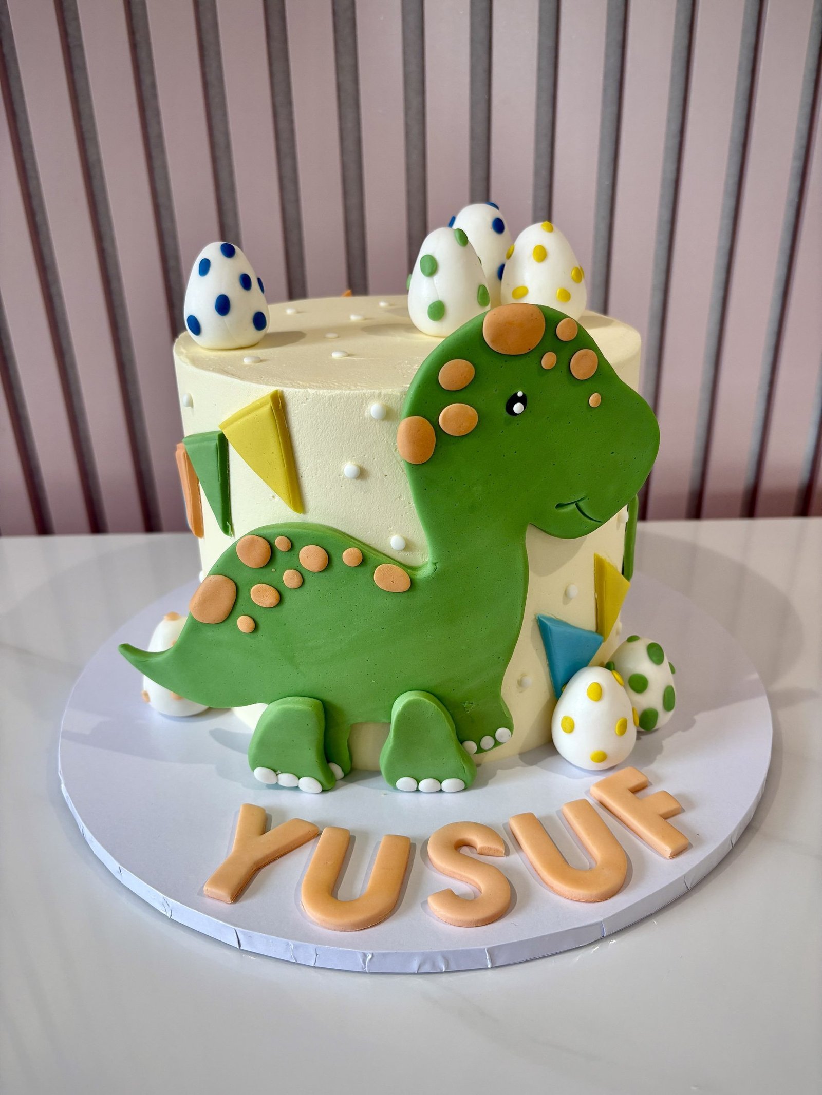 Cute green dinosaur birthday cake with fondant dinosaur, colourful spotted eggs and soft buttercream finish