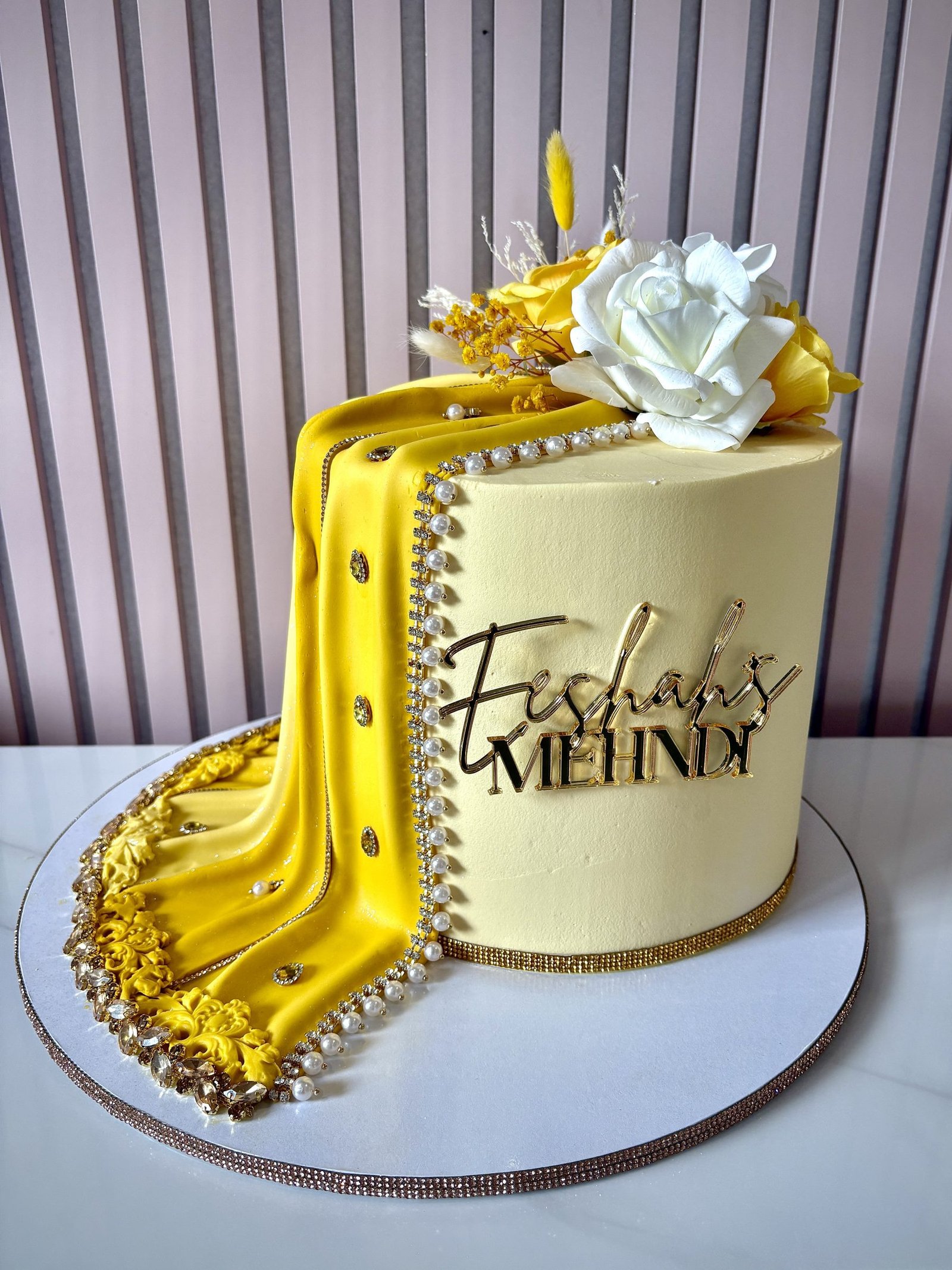 Yellow mehndi cake with draped design, pearl detailing, gold accents and floral decoration