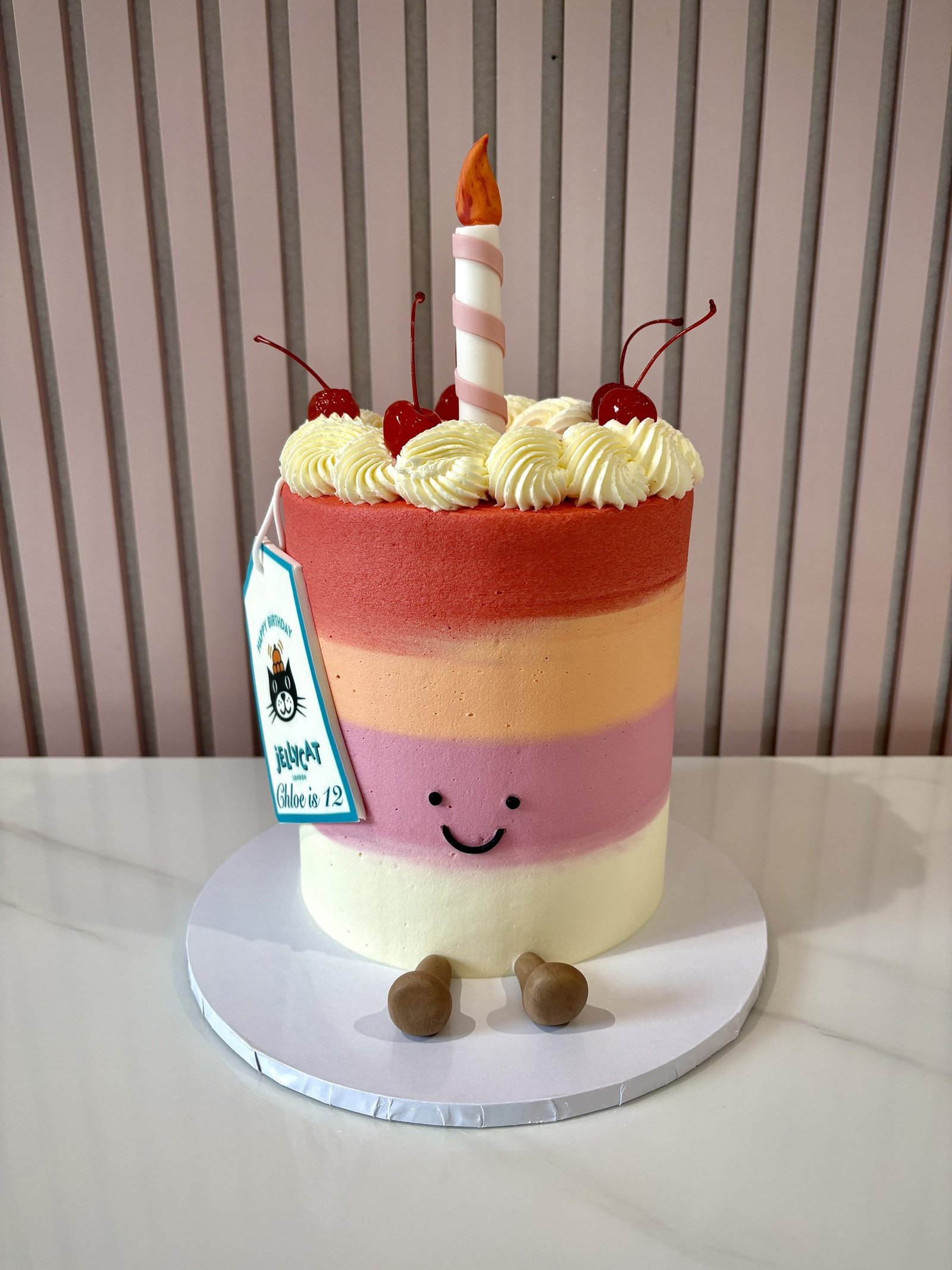 jellycat style birthday cake with pastel stripes, smiley face and candle topper