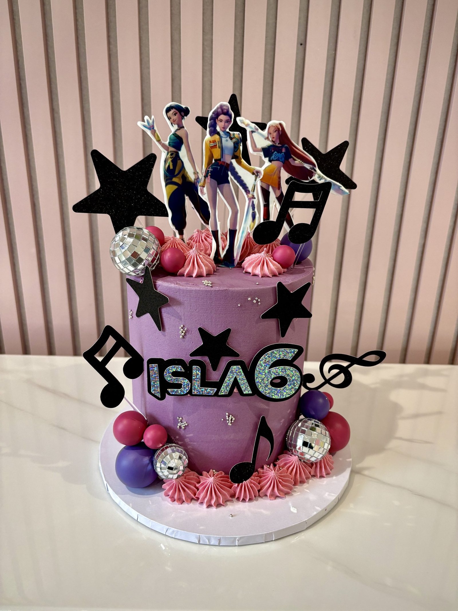K-pop themed birthday cake with character toppers, music notes, stars and pink and purple design