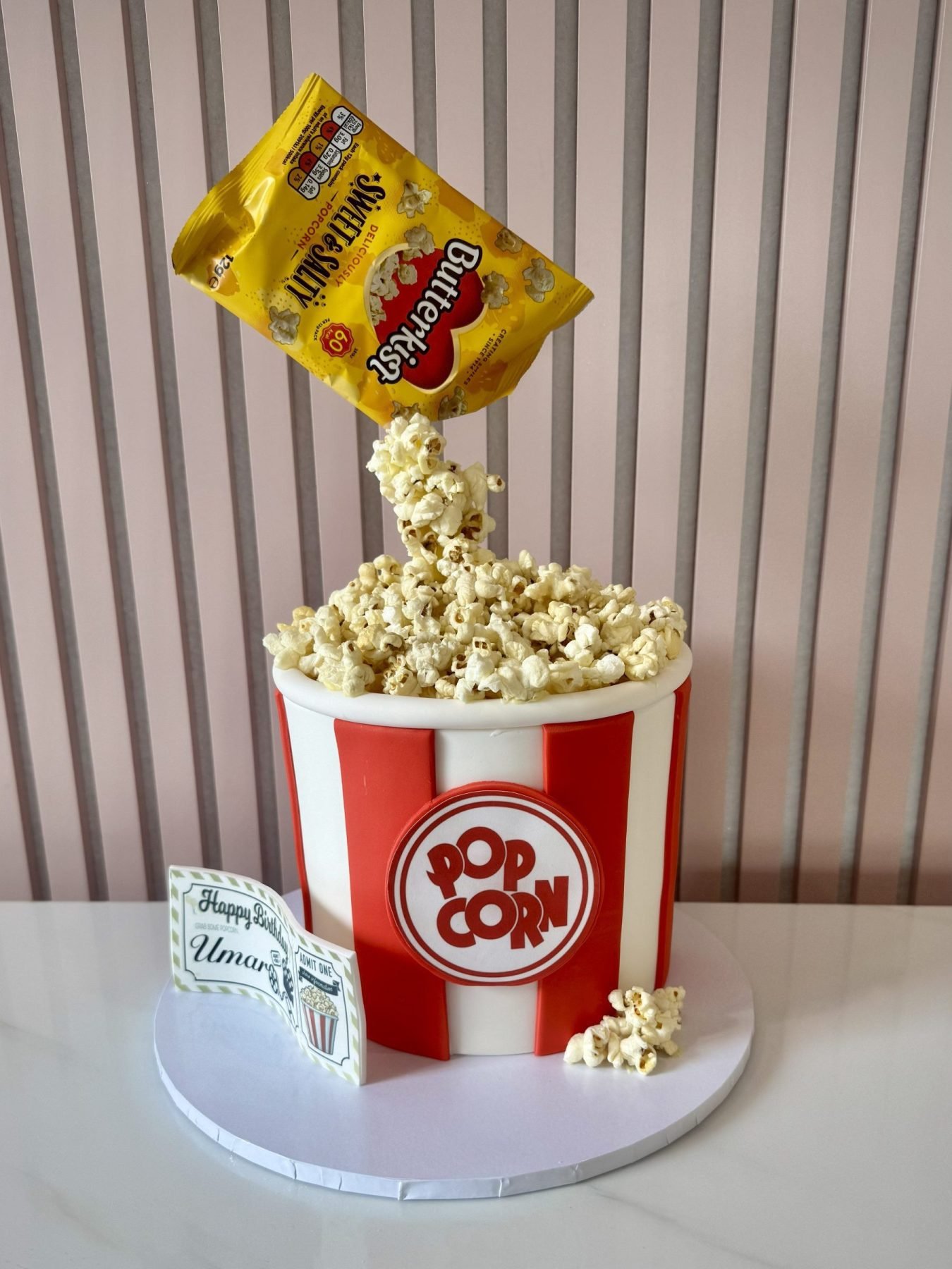Popcorn gravity birthday cake with red and white bucket design and floating popcorn effect from bag