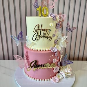 Two tier pink and ivory butterfly birthday cake with decorative flowers, pearl borders and butterfly decorations.