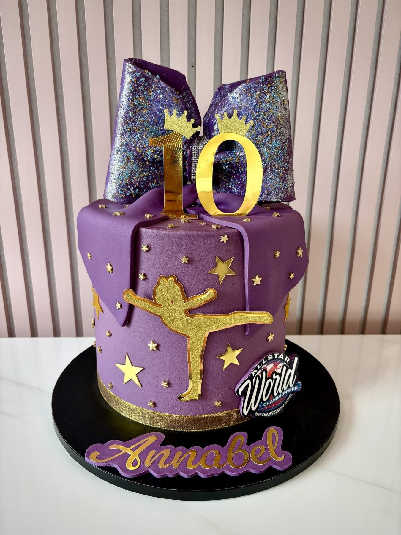 Purple cheerleader birthday cake with glitter bow topper, gold stars and cheerleader silhouette decoration.