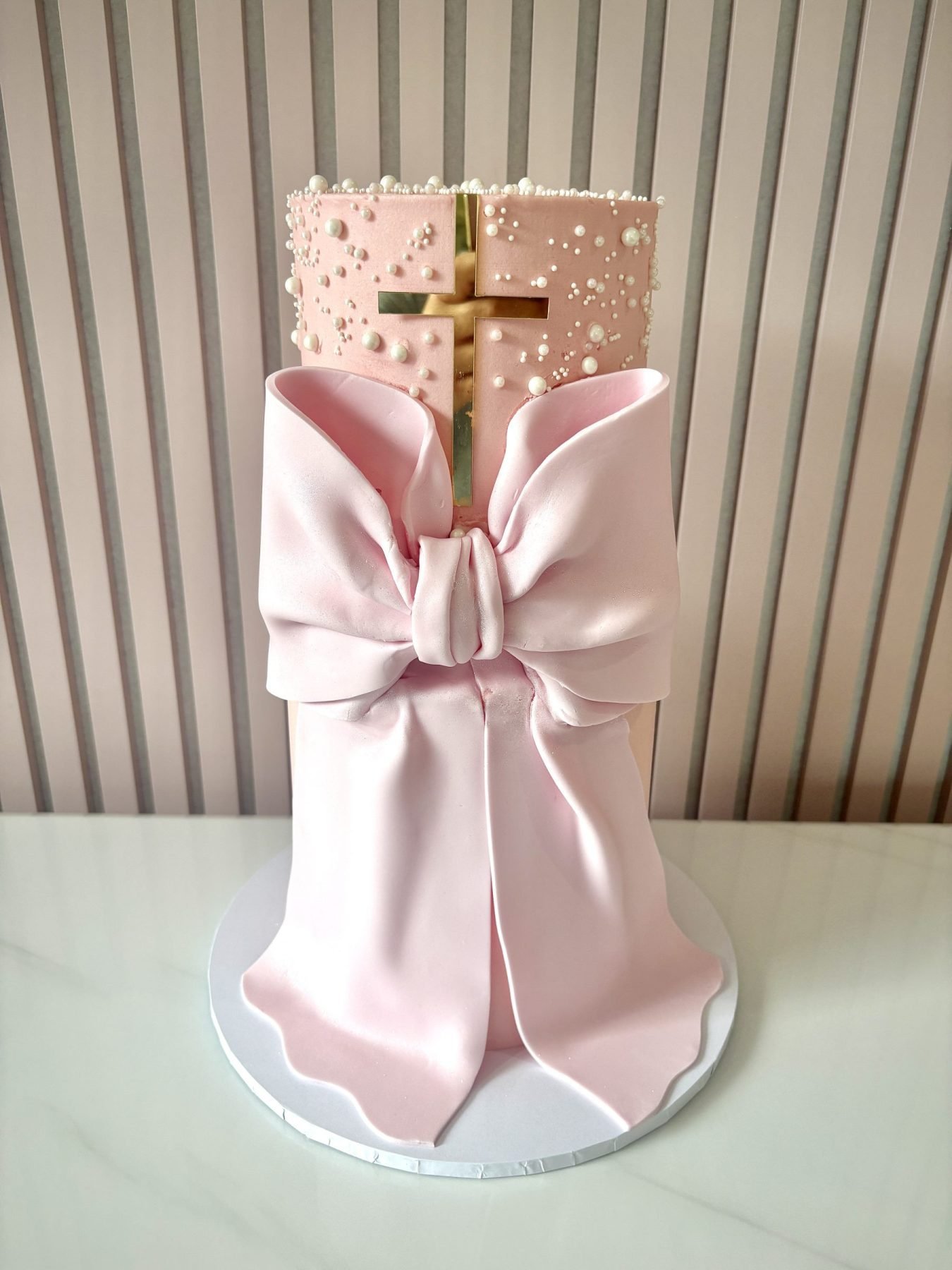 Elegant christening cake with fondant bow drape and gold cross detail