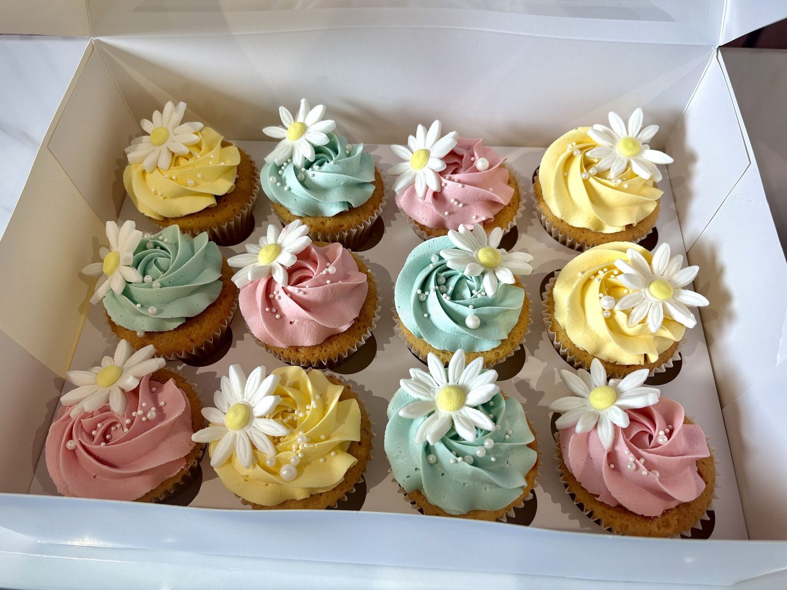 Pastel daisy cupcakes with pink yellow and mint buttercream swirls, floral toppers and pearl sprinkles
