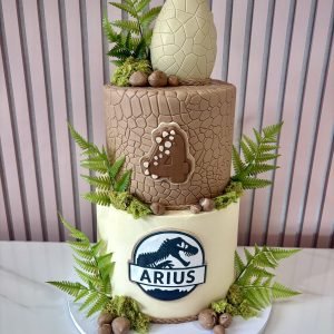 Two tier dinosaur birthday cake with textured fondant finish, greenery and dinosaur egg topper