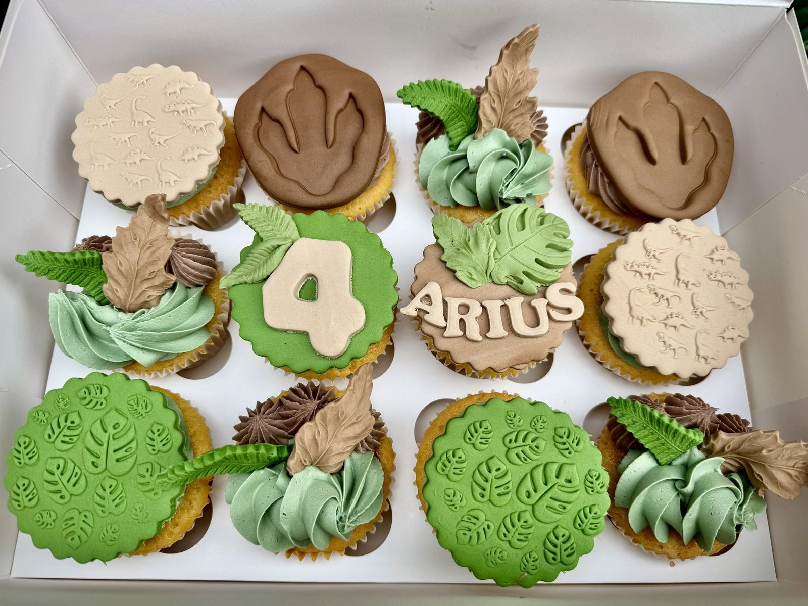 Dinosaur themed cupcakes with green buttercream, fossil toppers, jungle leaves and personalised name and age design