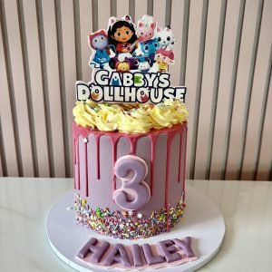 Gabby's Dollhouse themed birthday cake with pink drip icing, colourful sprinkles and character topper.