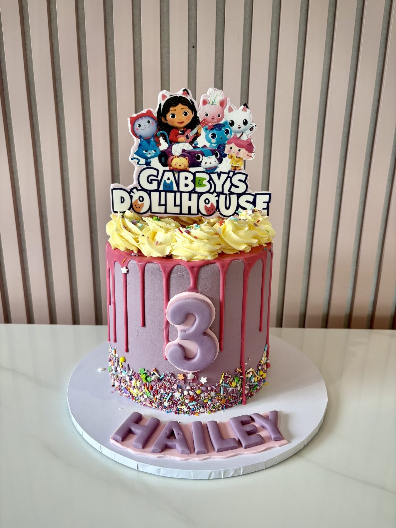 Gabby's Dollhouse themed birthday cake with pink drip icing, colourful sprinkles and character topper.