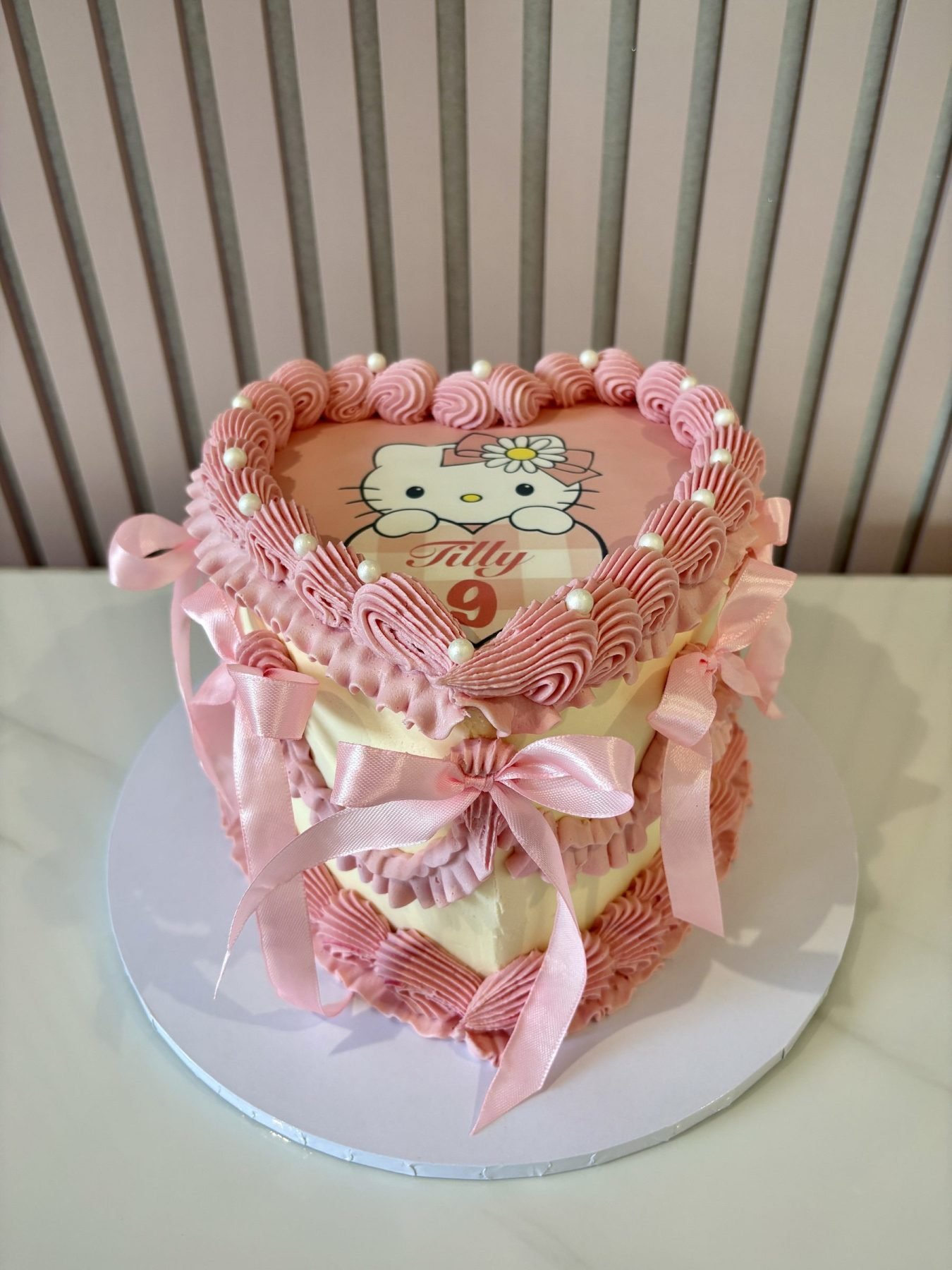 Heart-shaped Hello Kitty birthday cake with pink vintage piping, ribbon bows and personalised Hello Kitty topper.