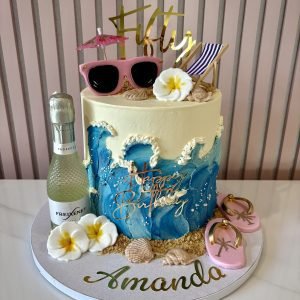 Holiday-themed cake with ocean waves, tropical flowers, flip-flops, sunglasses, prosecco and beach-inspired decorations.