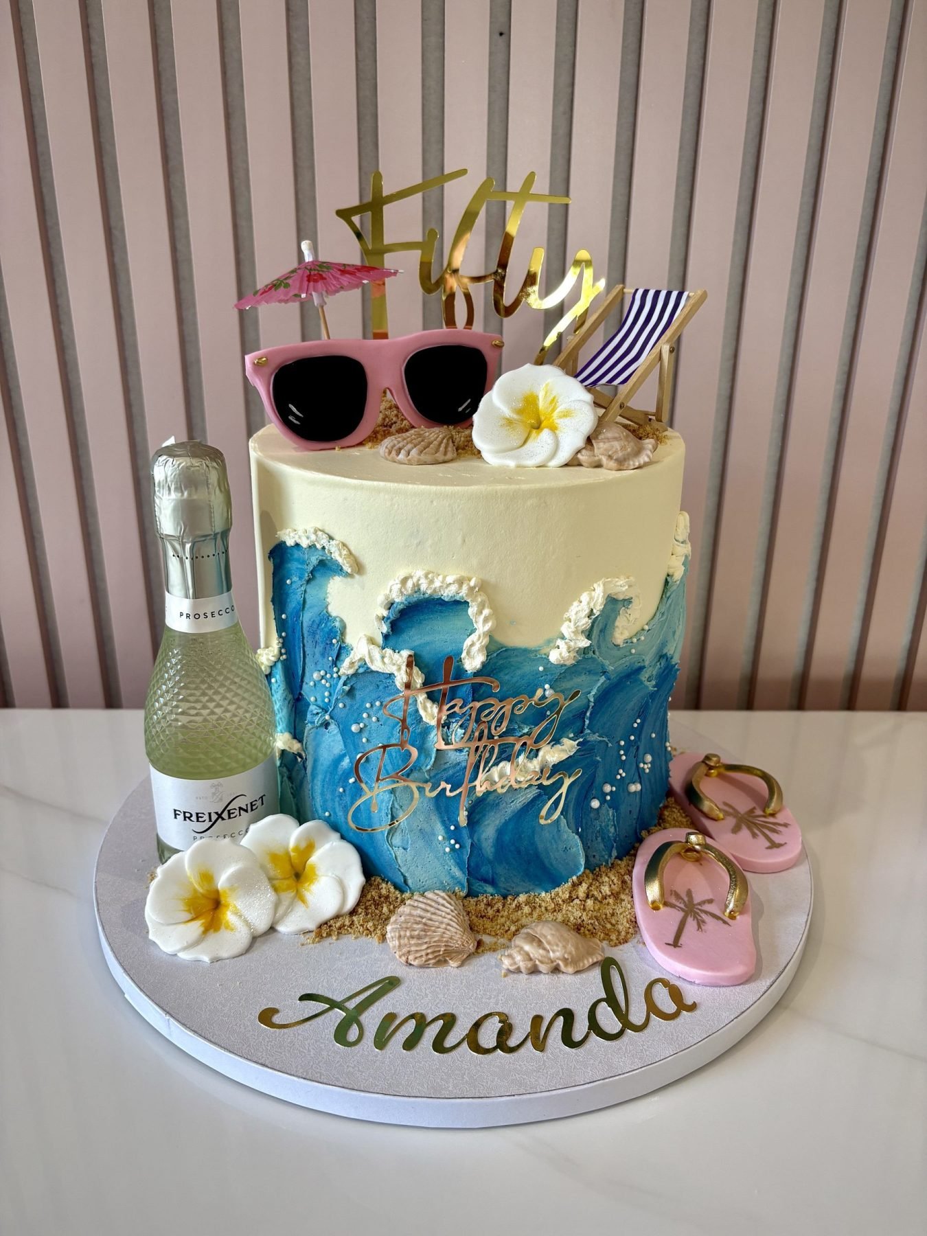 Holiday-themed cake with ocean waves, tropical flowers, flip-flops, sunglasses, prosecco and beach-inspired decorations.
