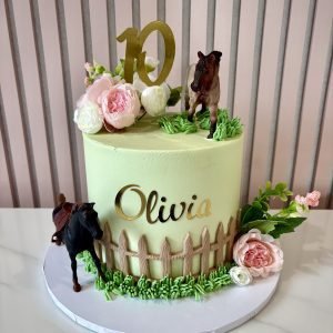 Horse themed birthday cake with green buttercream, horse figures, fence detail and floral decorations