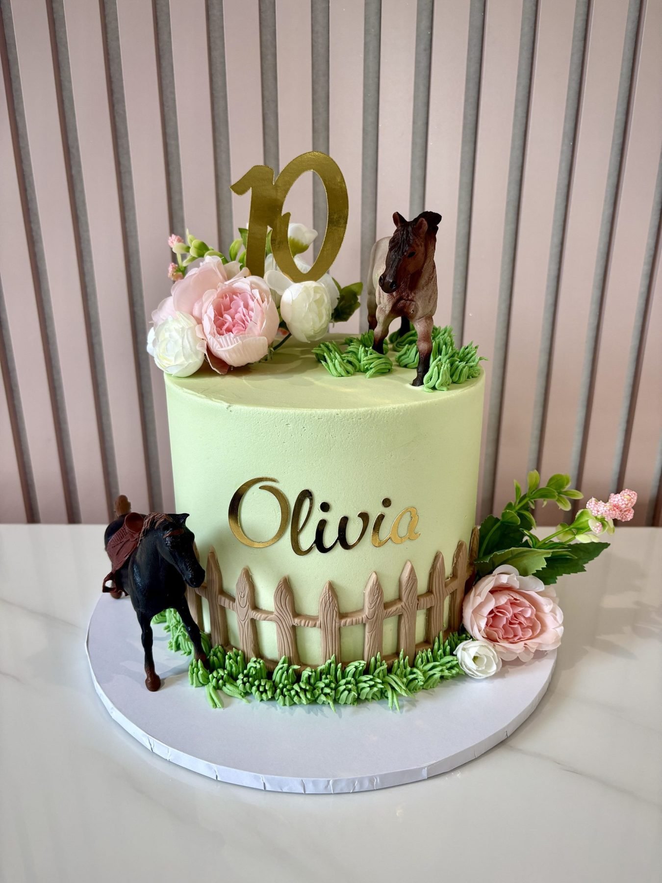 Horse themed birthday cake with green buttercream, horse figures, fence detail and floral decorations