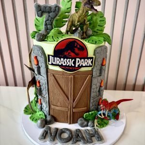 Jurassic Park inspired dinosaur birthday cake with jungle leaves, dinosaur figures and stone-effect details