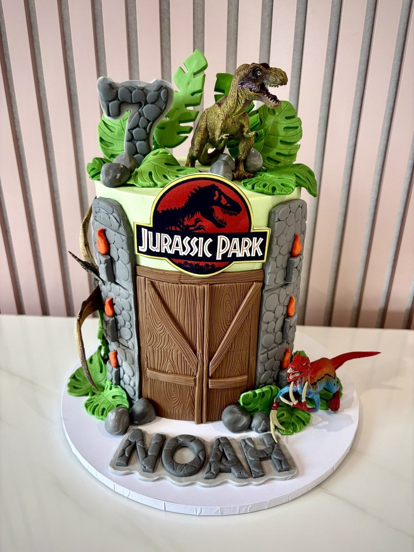Jurassic Park inspired dinosaur birthday cake with jungle leaves, dinosaur figures and stone-effect details