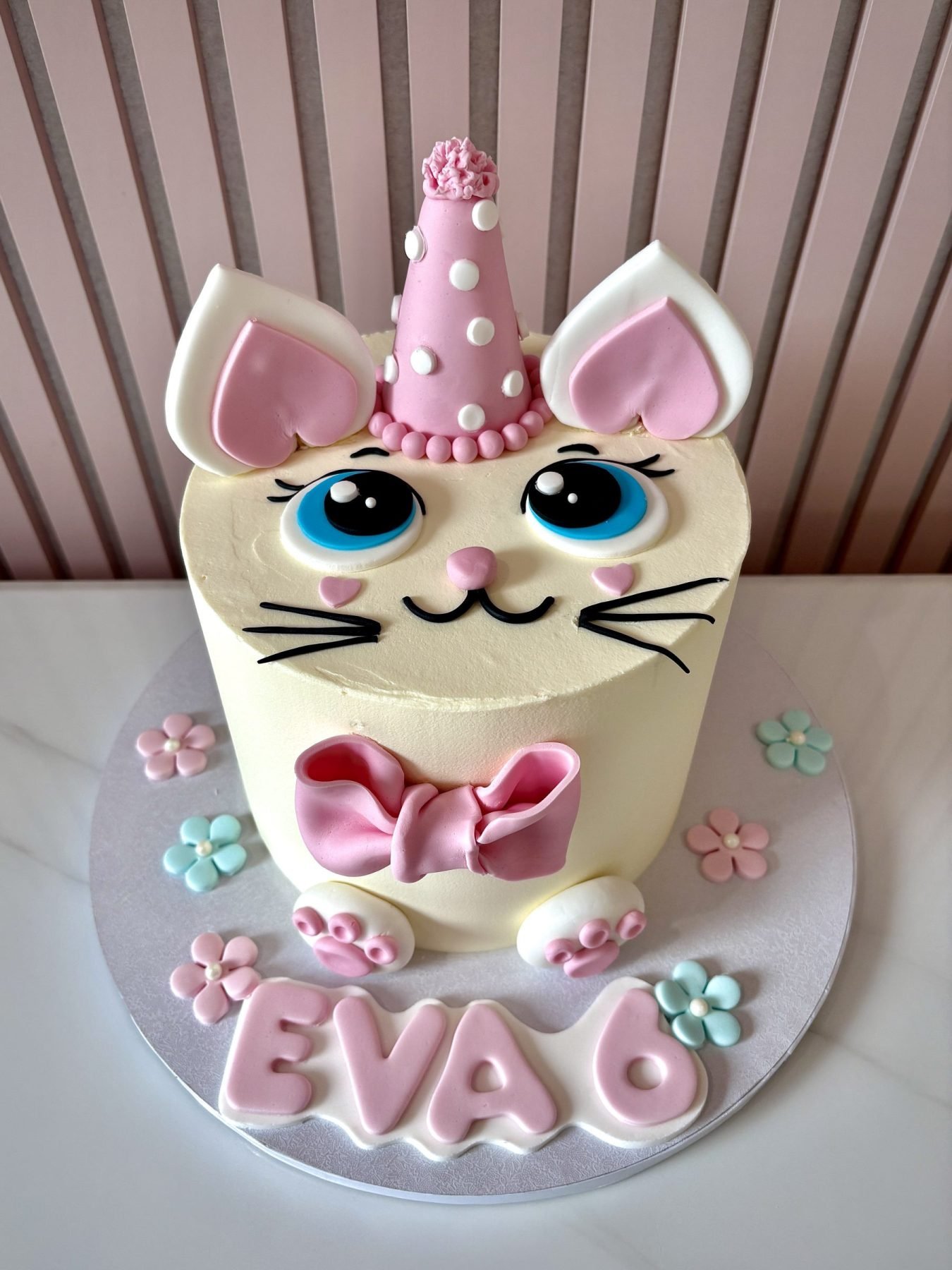 Pastel kitty birthday cake with fondant cat face, pink bow, pastel flowers and unicorn style horn