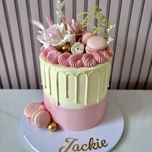 Pastel pink and ivory drip cake decorated with macarons, blush roses, buttercream swirls and gold accents.