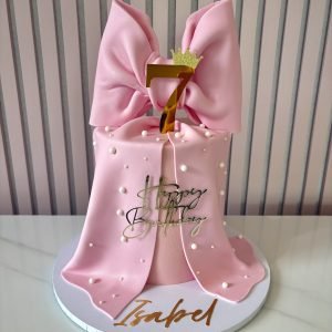 Pink birthday cake with a large handcrafted bow, pearl detailing and a customisable age topper.