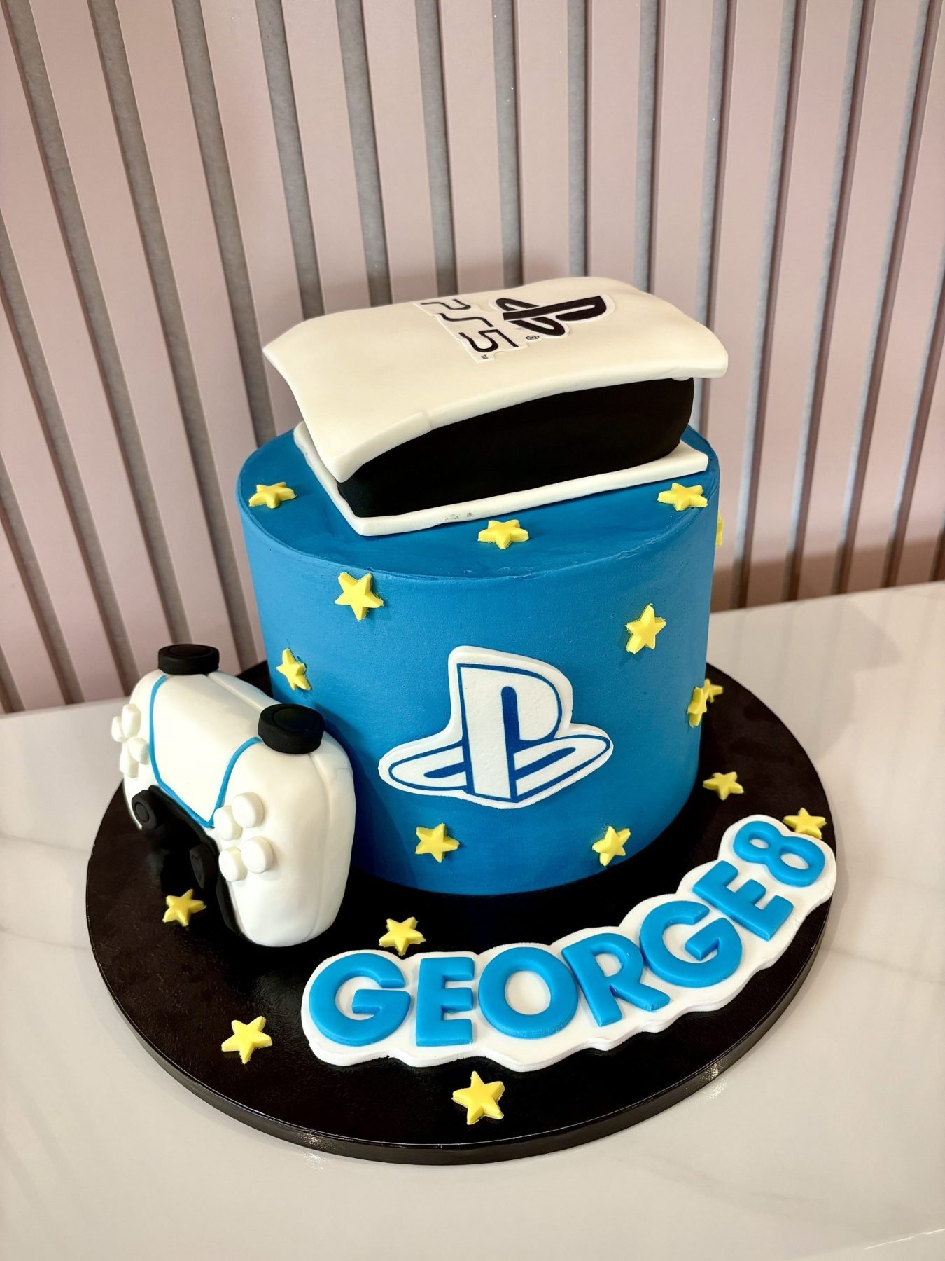 PlayStation themed birthday cake with PS5 console topper, controller and blue gaming design