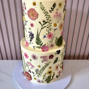Two tier buttercream cake decorated with colourful pressed flowers and botanical details