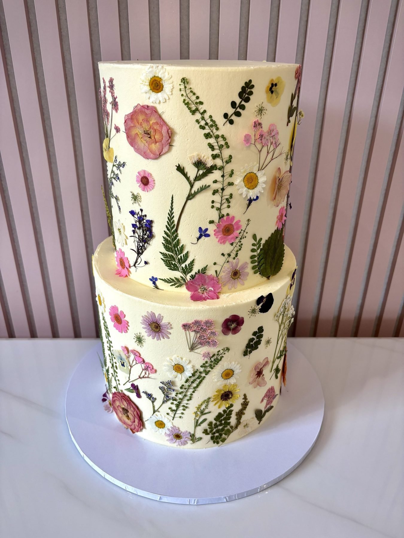 Two tier buttercream cake decorated with colourful pressed flowers and botanical details